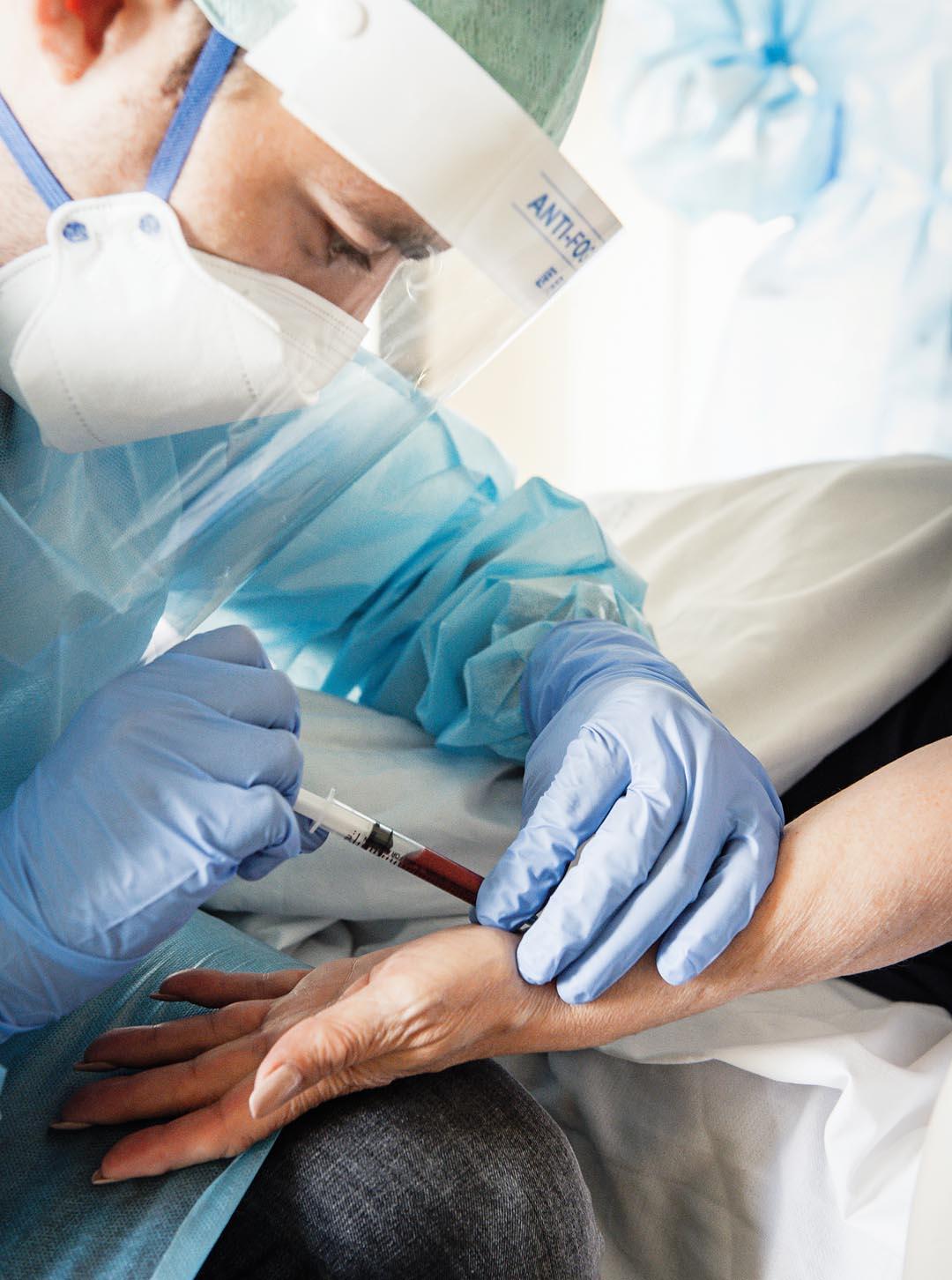 Een dokter met masker doet een bloedafname bij een patiënt