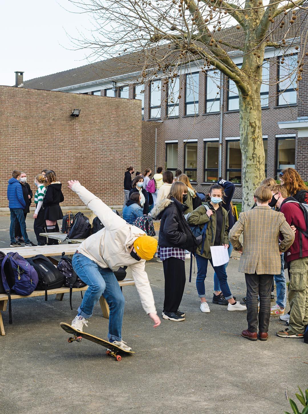 Des jeunes se parlent sur le terrain de jeu  et un garçon fait des manoeuvres sur son skateboard