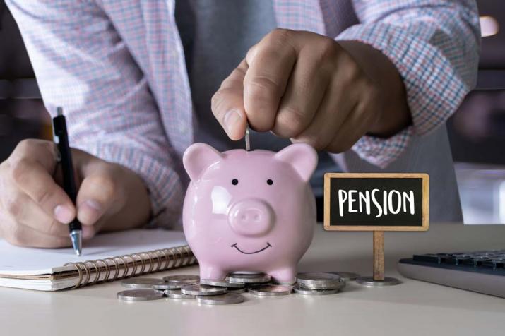 Pensioenen: een man steekt enkele muntstukken in een spaarvarken voor zijn toekomstig pensioen  terwijl hij zijn uitgaven berekent