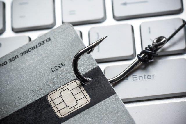 Fraud: a credit card attached to a fishhook lying on a keyboard